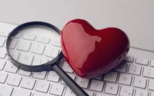Czerwone serce i szkło powiększające spoczywają na białej klawiaturze komputera. Speed dating Warszawa