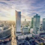 Panorama z lotu ptaka centrum Warszawy z wysokimi biurowcami, na tle zachodzącego słońca.