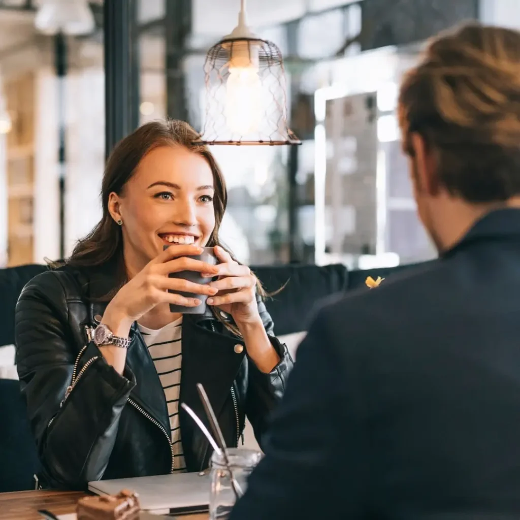 kobieta i mężczyna siedzą przy stole w kawiarni, kobieta w czarnej kurtce, prowadzą rozmowę, są uśmiechnięci, spotkanie Speed Dating u Amora, Warszawa, poznaj singla,