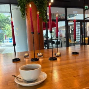 filiżanka kawy stoi na stole w kawiarni, obok palą się świece w kolorze różowym, miejsce spotkań speed dating u Amora, szybkie randki dla singli