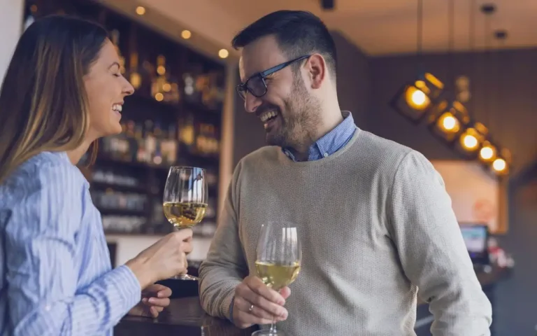 Uśmiechnięta kobieta i mężczyzna stoją przy barze w przytulnej, nowoczesnej restauracji, trzymając kieliszki białego wina i prowadząc swobodną rozmowę. Atmosfera radości, bliskości i relaksu podkreśla dobre samopoczucie oraz celebrowanie chwili, doceniając single warszawa szybkie randki dla dorosłych Warszawa