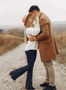 kobieta blondynka w kapeluszu, biała bluzka, dżinsy, przytula się do mężczyzna w brązowym płaszczu, na plaży, single Warszawa, szybkie randki u amora, single warszawa